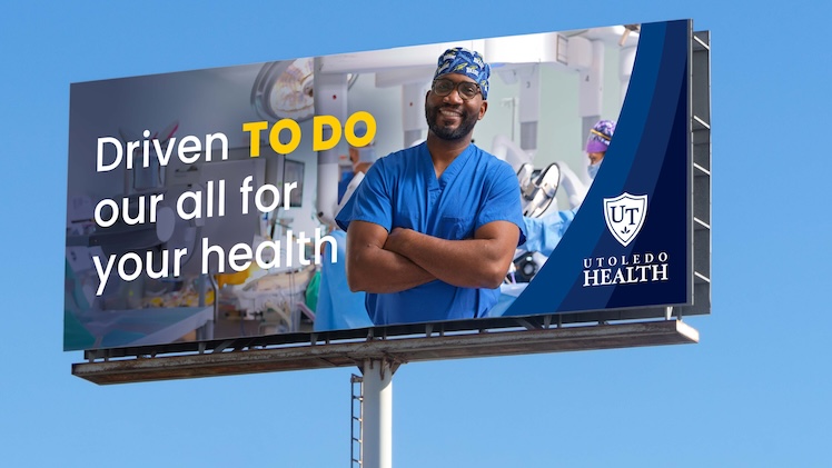 Outdoor billboard mockup featuring surgeon standing with arms crossed in an operating room with the words Driven TO DO our all for your health