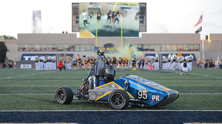 Tim Del Signore is behind the wheel of the racecar he and his Rocket Motorsports teammates designed and built last year to lead the Rockets football team into Glass Bowl Stadium before home games all season.