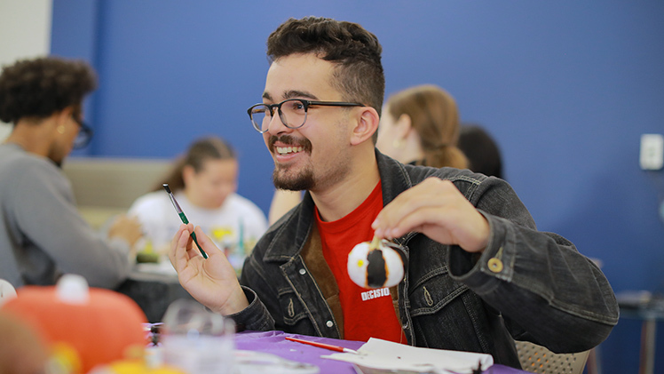 Stephen Ortiz, a freshman studying health science, shows off his decorating skills at the Mini-Pumpkin Painting Party on Wednesday in the Office of Multicultural Student Success Lounge. The event was cohosted by the Rocket Career Center and Office of Multicultural Student Success as part of the Rocket Career Center’s “BOO-sting Your Career Week” Halloween-themed activities.