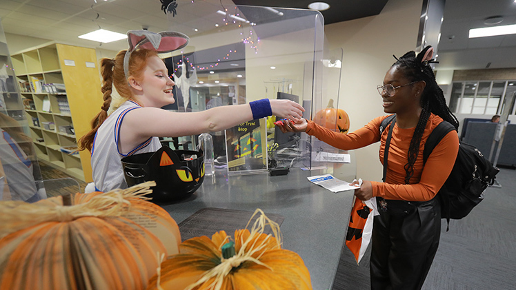 Linnea Bell, a sophomore double major in cosmetic science and formulation design and Spanish, gives candy to trick-or-treater Laila Fitzpatrick, a second-year pharmacy student, at the Carlson Library Trick or Treat event on Halloween.