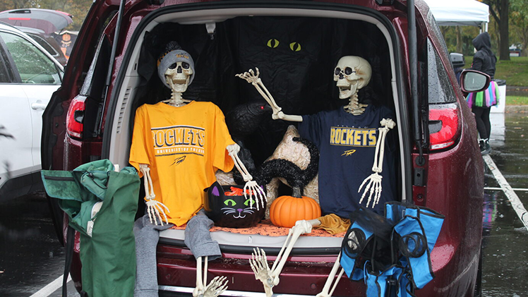 Photo of two plastic skeletons dressed in Rocket gear seated in a back of an SUV trunk during UToledo Health's community trunk-or-treat event.