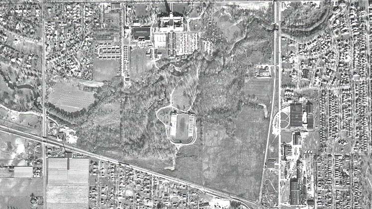 This aerial photo by the Lucas County Auditor’s Office captures UToledo’s Main Campus as it appeared in 1950: University Hall at top center, World War II-era military barracks south of the building, a grass parking lot that replaced a baseball diamond to the east of University Hall, and the football stadium, newly renovated and renamed “The Glass Bowl,” at the southern part of campus. Wending through the heart of campus is the Ottawa River.