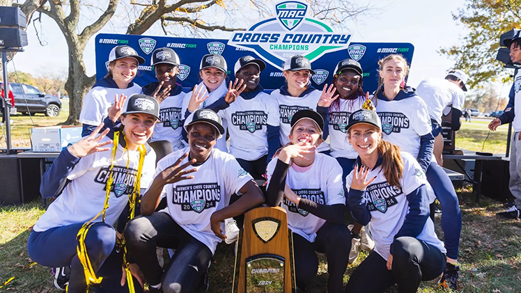 Group photo of Toledo Women's Cross Country team celebrating as they pose for the photo after they won their fourth-consecutive MAC Championship, a first for the program.