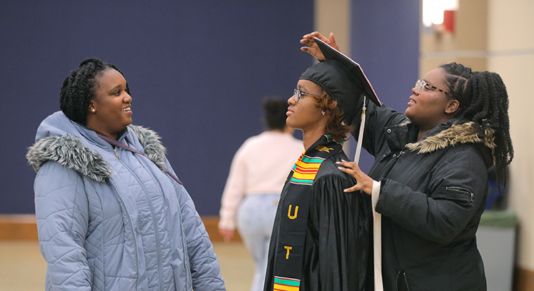 Tammie Watkins, left, watches as her niece Kemeiah Mcclorrine adjusts the graduation cap of her twin sister, Kemyiah Mcclorrine, a psychology senior, before the ceremony.