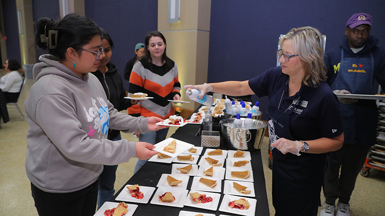 Dr. Julie Fischer-Kinney, executive director of student experience, adds whipped cream to the pie of Kristi Shrestha, a graduate student in chemistry during the President’s Thanksgiving Lunch in November.