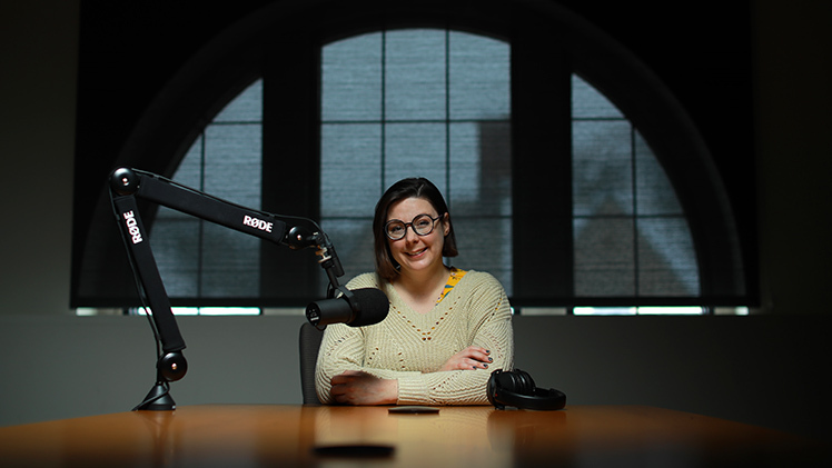 Portrait of Dr. Rebecca Monteleone, an assistant professor in the Disability Studies Program, at a desk with a large microphone. She co-hosts the podcast Telling It Our Way on WGTE.