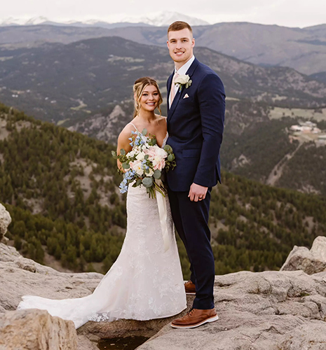 Anthony Torres poses with his wife, Taylor, in their wedding attire with the scenic mountains of Colorado in the background.