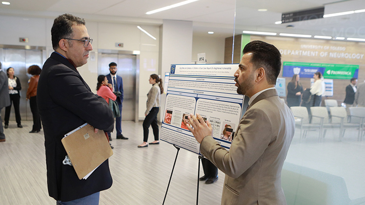 Dr. Amin Sanei Moghaddam, a clinical assistant professor in the College of Medicine and Life Sciences, listens to UToledo research assistant Gulbudin Muhammad talk about his group's research, “Dog Bites and Epilepsy in Children,” as he judges poster presentations during the 3rd Annual Research Day, sponsored by the Department of Neurology.