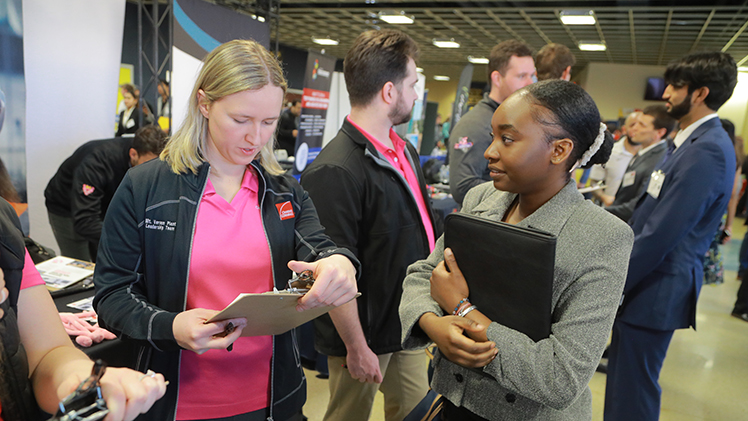 A female UToledo engineering senior talks with a female recruiter at the Spring 2024 Engineering Career Expo in Savage Arena.