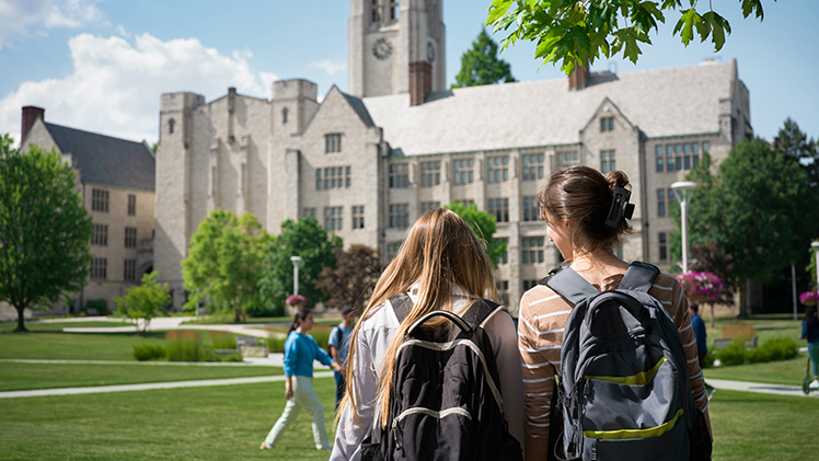 Photo from behind of 2 female UToledo students wearing backpacks as they walk across Centennial Mall.