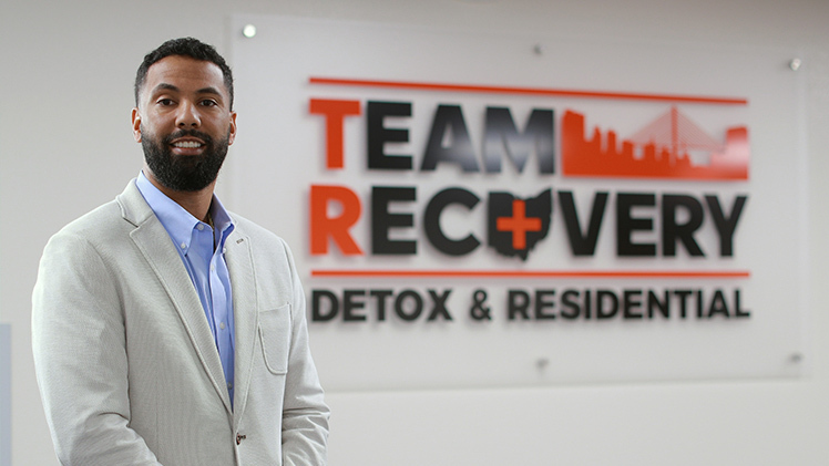 Matt Bell, who will graduate May 2 with his degree in social work, stands in front of a Team Recovery sign.