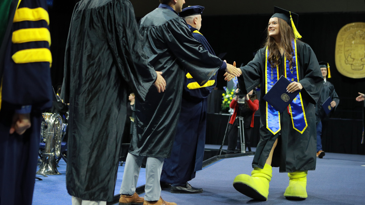 Jenna Muetze wears her a pair Rocky boots as she shakes hands with trustees. Muetze, who graduated with a bachelor of science degree in environmental sciences, was Rocky No. 83.