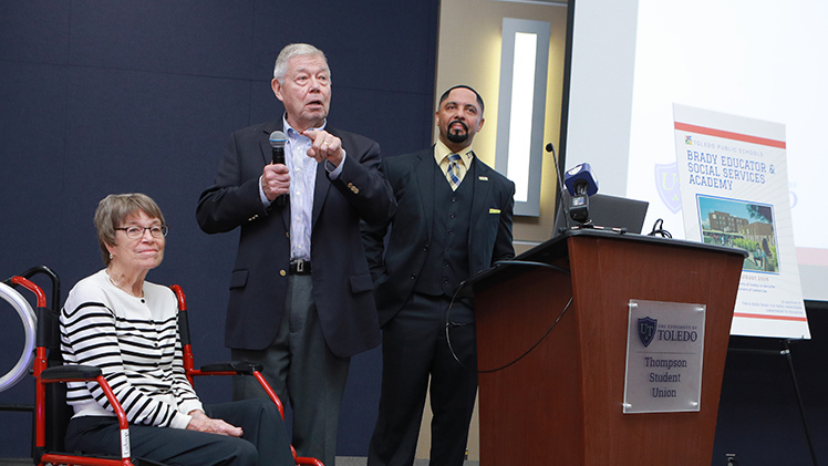 Photo of Tom and Betsy Brady and TPS Superintendent Romules Durant during the announcement. Tom Brady is holding a microphone and speaking.