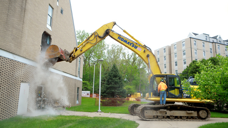 With Interim President Matt Schroeder at the controls, an excavator begins the demolition of the exterior of the academic office building Sullivan Hall on Thursday.