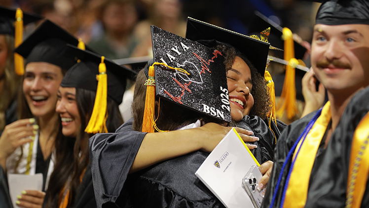 Mabely Acevedo, facing the camera, and Jaya Bhatnagar, both of whom graduated with bachelor of science in nursing degrees, hug during the morning commencement ceremony.