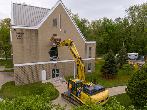 Drone photo of an excavator as it it begins demolition of the exterior of Sullivan Hall.