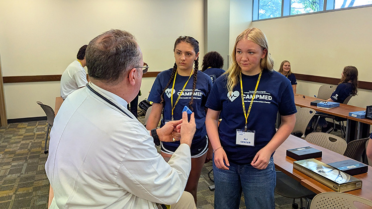 Anabella Miller, center, and Ali Genter, right, listen as Dr. Paul Schaefer, a UToledo Health internal medicine specialist, explains how to use a reflex hammer to assess the nervous system last week at CampMed.