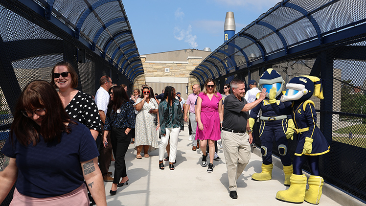Pedestrians including Rocky and Rocksy cross over the new pedestrian bridge over Douglas Road.
