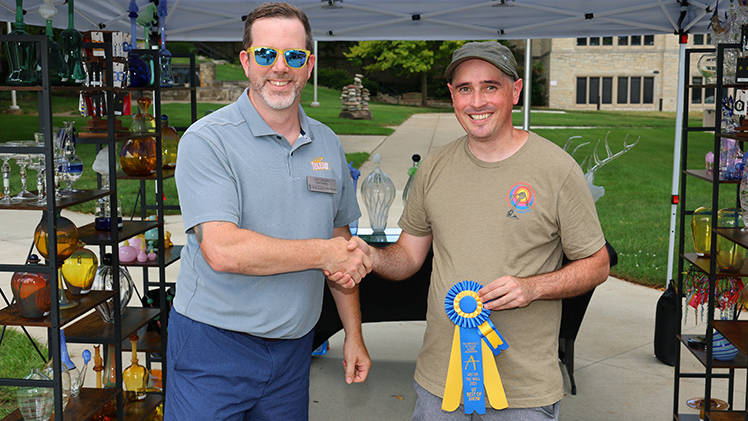 Matt McClure, University of Toledo Alumni Association Board President, congratulates local artist Eamon King, a scientific glassblower at UToledo, for winning the Best of Show Award at Sunday’s 32nd Art on the Mall.
