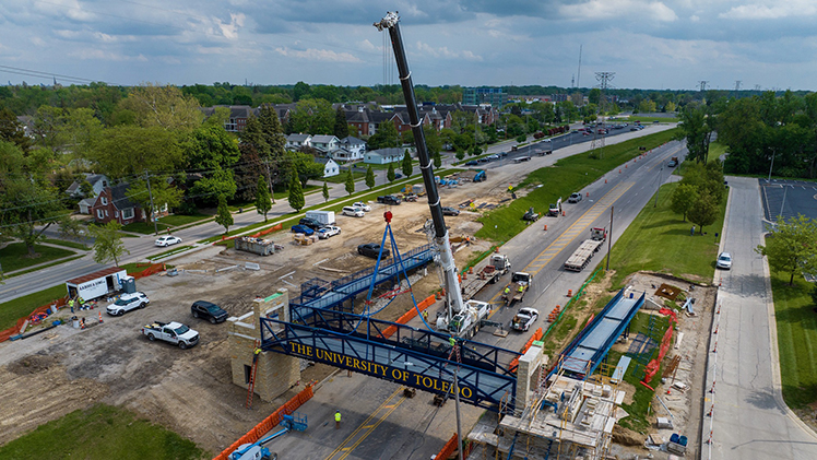 Drone photo of the new footbridge that better connects The University of Toledo’s engineering complex to the heart of Main Campus across Douglas Road as it is being put into place in May 2025.