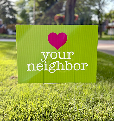 Photo of Love Your Neighbor yard sign planted in someone's yard. 