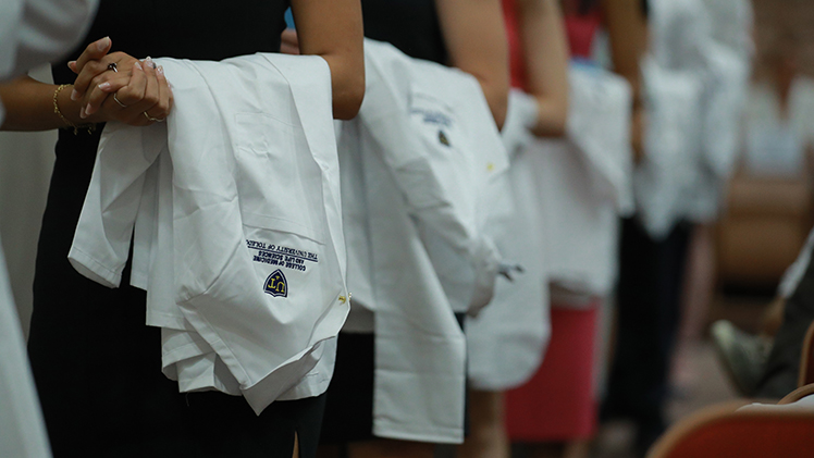 Close-up photo of UToledo medical students standing in line with their white coats draped on their arms during a white coat ceremony.