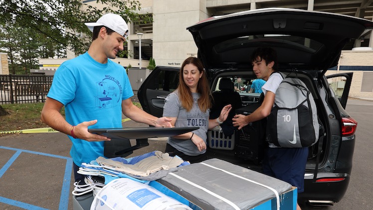Braden Vineyard a UToledo nursing student, loads a TV into a moving cart for first-year psychology Nathan Stubleski, as his mom, Ashleigh Stubleski — a UToledo graduate and UToledo Health physical therapist — looks on.