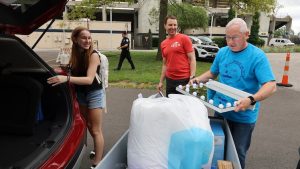 UToledo President James Holloway loads a lighted vanity into a moving cart as first-year student Nicole Zanko and her dad, Larry Zanko, watch.