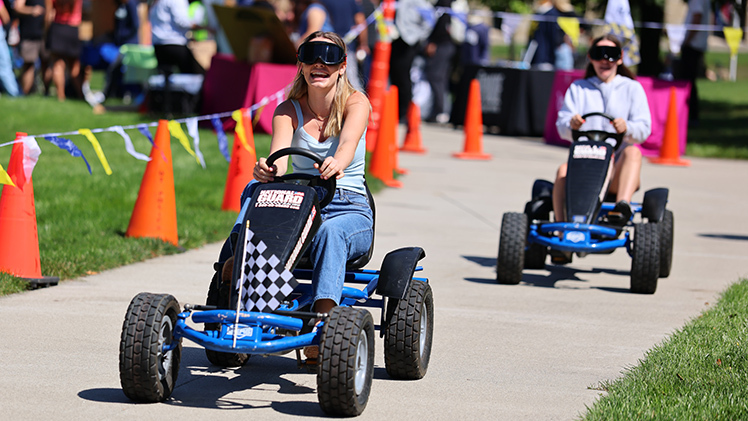Emily Swartz, a sophomore in nursing, leads her friend, Annie Mauk, a sophomore in nursing, on pedal carts while wearing drunk-driving simulator goggles from The University of Toledo Police booth at Wednesday’s Campus Involvement Fair at Centennial Mall.