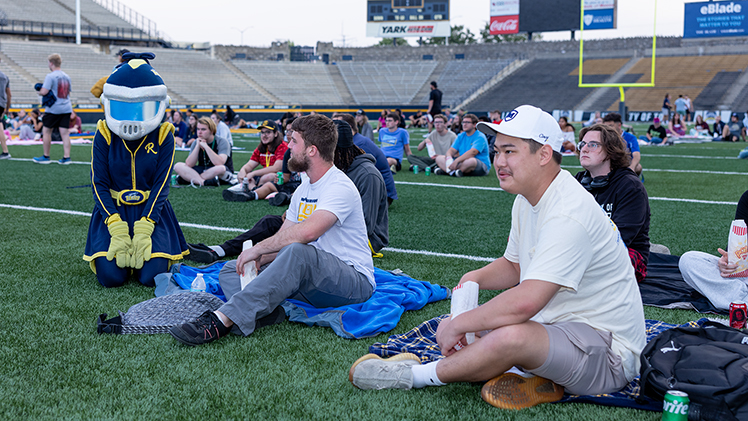 Caleb Wrobel, left, a freshman studying astrophysics, and Matt Arand, a freshman in special education, sit with Rocksy as they wait for "A Minecraft Movie" to begin at the Flicks on the Field event Saturday night at the Glass Bowl. 