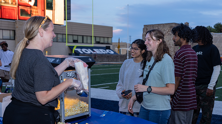 Diya Dhyani, a senior bioengineering major, and Emily Bella, a senior studying communication, stand in line to get popcorn from Sara Clark, assistant dean of students.