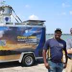 Dr. Kennedy Doro and Dr. David Kennedy stand in front of UToledo's trailer-mounted atmospheric sampling platform at the Lake Erie shoreline.