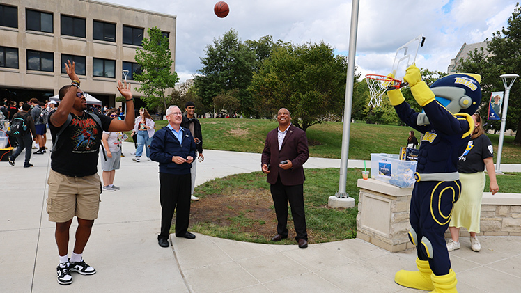 Marquan Denby, a senior in communication, shoots a basketball for prizes as President Holloway and Vice Provost and Dean of Students Sammy Spann and Rocky watch.