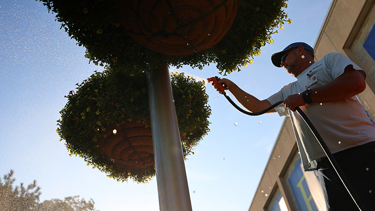 In the waning days of a hot summer, grounds maintenance manager Jeff Gajdostik waters the hanging flower baskets in Centennial Mall.
