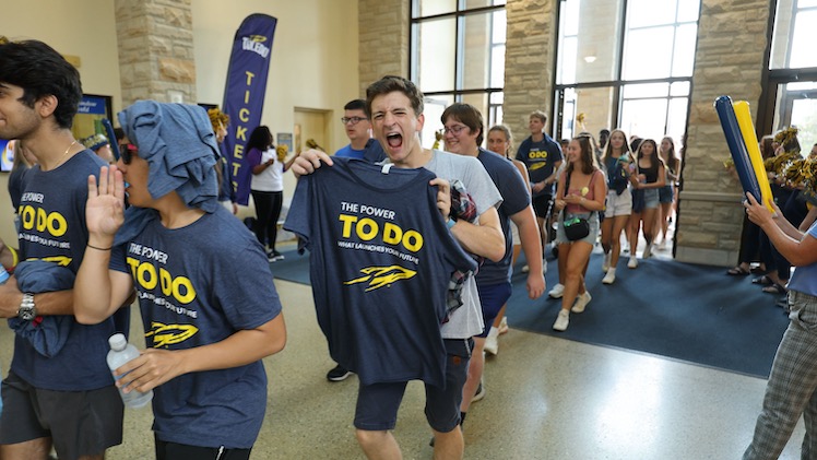 A male UToledo student excitedly holds up a "The Power To Do" shirt during UToledo's new student convocation.