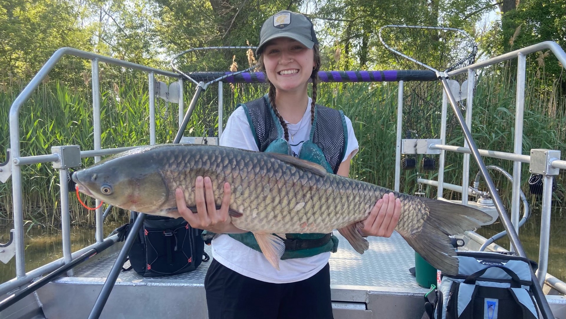 Shelby Adkins, a 2024 UToledo graduate, stands on a boat and holds a large grass carp she caught.