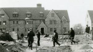 Several construction workers stand in front of Tucker Hall in a historic black and white photo.