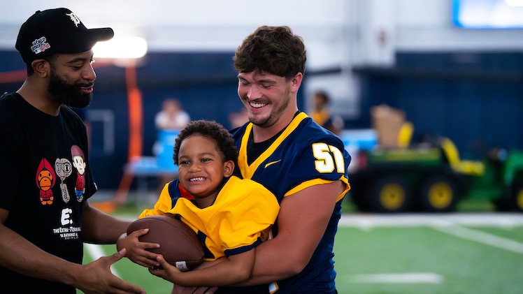 Owen Gibbs, a senior linebacker, holds a smiling boy during Victory Day on Saturday, Aug. 16.