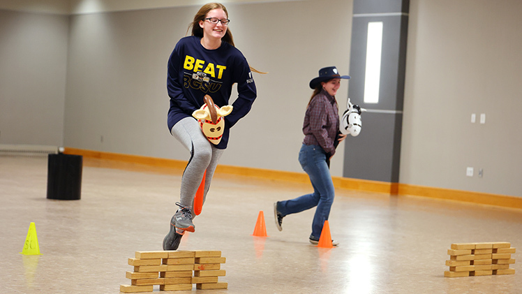 Zoe Bacorn, a sophomore in education, and Reyna Kelly, a sophomore in social work, ride hobby horses as they race against each other on a competition course set up in Thompson Student Union Ingman Room.