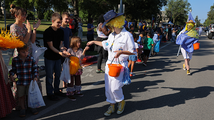 A member of the UToledo Blue Crew dressed as a clown hands out candy to children during the Homecoming Parade.
