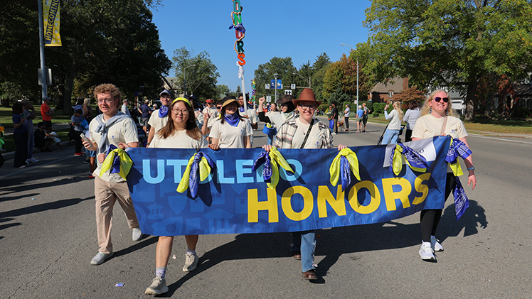 Students in the Honors College holding a "UToledo Honors" banner march in the Homecoming Parade.