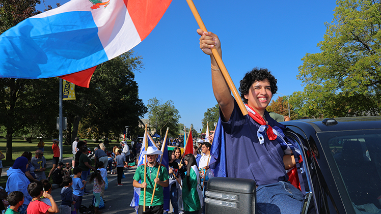 A UToledo student waves a flag while sitting in a pickup truck as part of the Homecoming Parade.