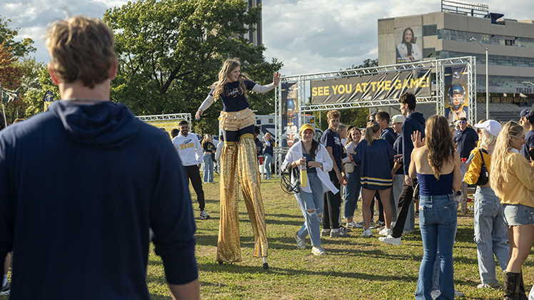 A UT cheerleader walks on stilts in front of a pre-game ceremony crowd.