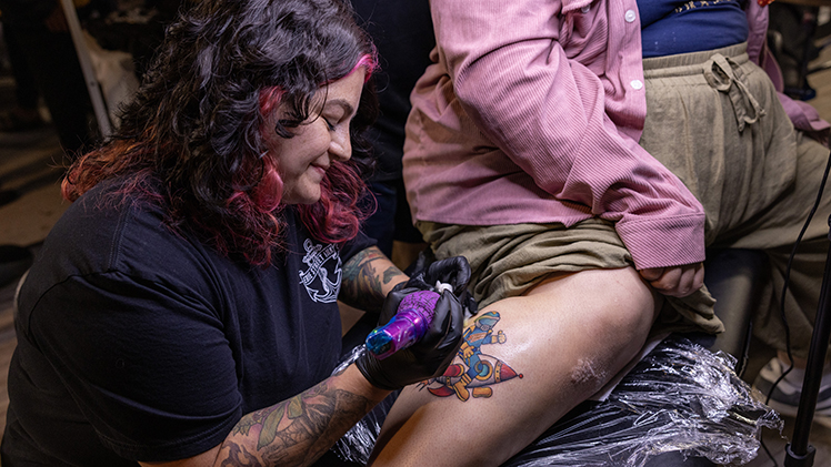 A female tattoo artist inks Rocky on a fan during a pre-game activity.