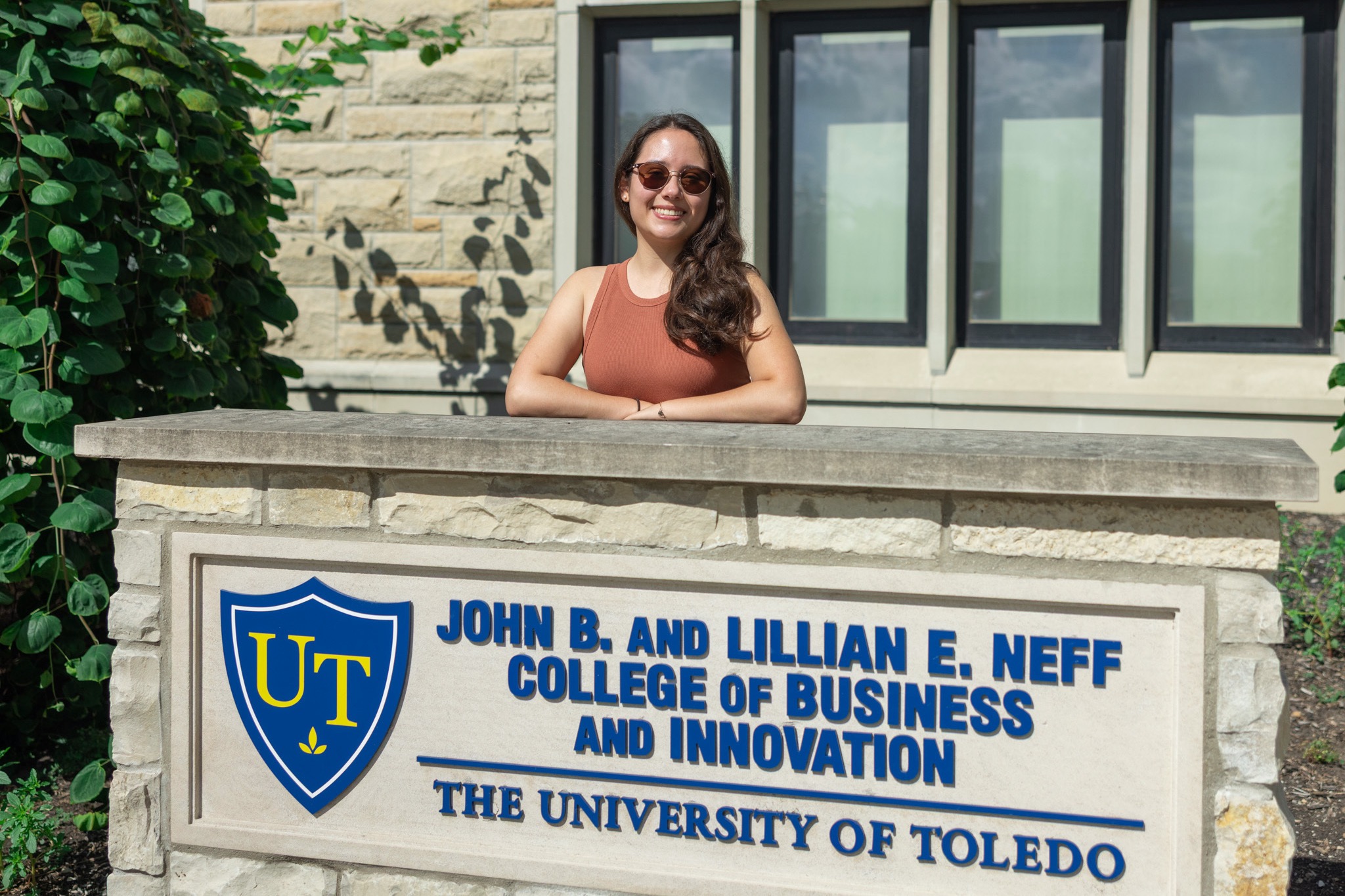 Ailean Arias Gutiérrez, a senior finance major, stands behind the John B. and Lillian E. Neff College of Business and Innovation sign on UToledo's campus. 
