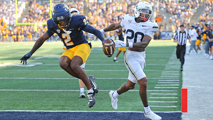 Toledo player jumps into the end zone while holding the football out to the side. 