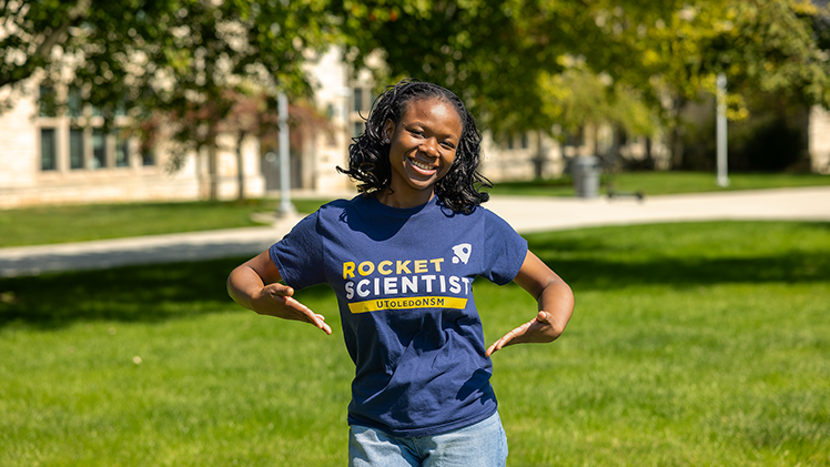 Outside portrait of UToeldo biology student Favour-Ohaezu who is wearing a "Rocket Scientist" T-shirt.