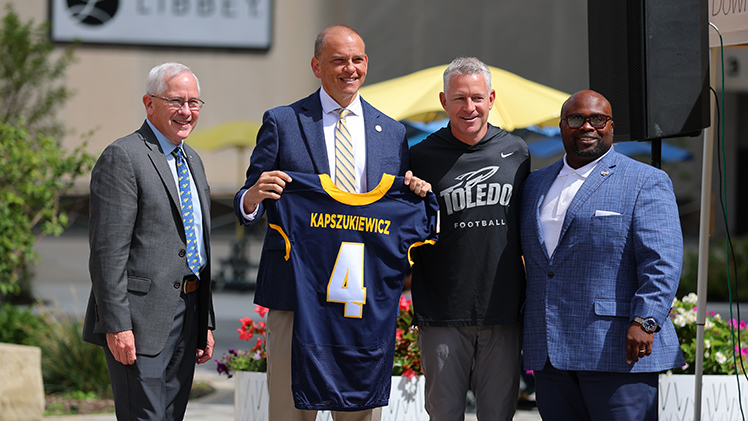 UToledo President James Holloway, from left, Toledo Mayor Wade Kapszukiewicz, Toledo Football Head Coach Jason Candle, and Vice President for Intercollegiate Athletics and Director of Athletics Bryan Blair pose after presenting the mayor with his own UT football jersey at a Thursday afternoon downtown pep rally in Levis Square.