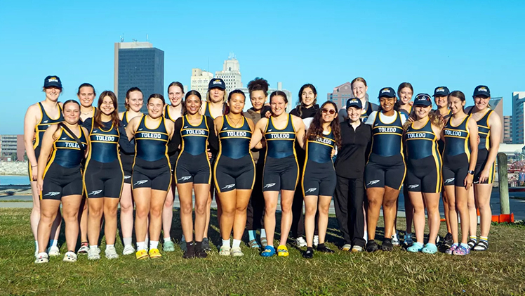 Posed group photo of the UToledo Women's Rowing team at a practice at the Maumee River in downtown Toledo.