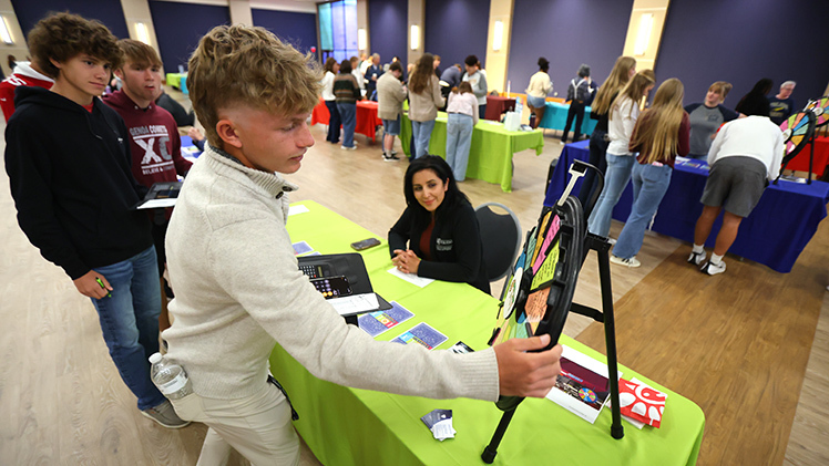 Maryam Sediqe, assistant director of UToledo’s Center for International Studies and Programs, watches as Genoa High School’s Colby Ralston of spins a wheel during Finances 101.